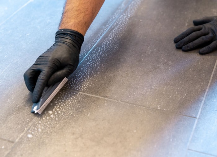 Nettoyage des joints sur les carreaux gris à l'aide d'une brosse à récurer et de gants.