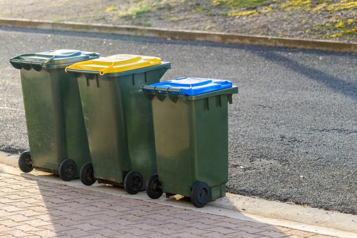 Trois poubelles et bacs de recyclage en bordure du trottoir devant une maison.