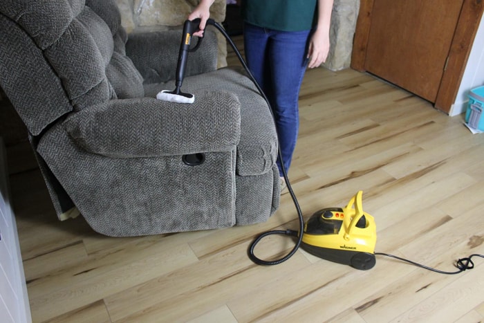 Une femme nettoie à la vapeur l'accoudoir d'un fauteuil inclinable gris