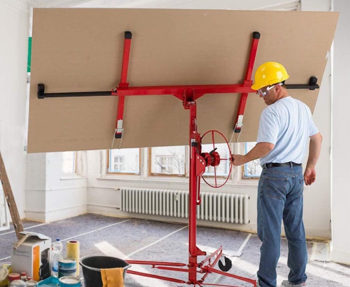 Une personne utilise le palan pour panneaux de cloisons sèches FDW pour maintenir un grand panneau de cloisons sèches dans une pièce en cours de rénovation.