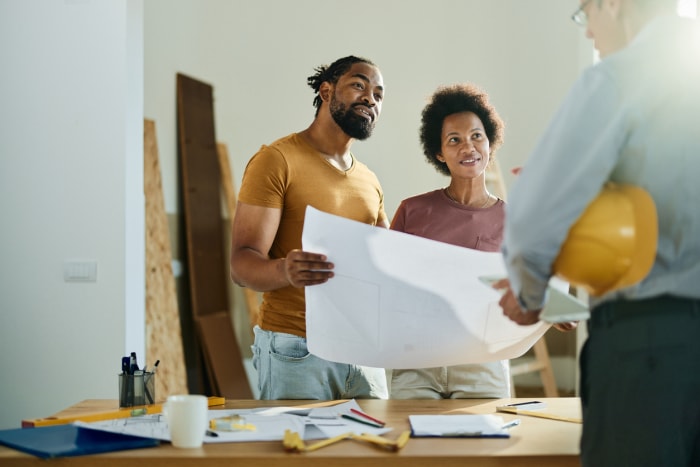 Un heureux couple afro-américain analyse des plans tout en communiquant avec un entrepreneur en bâtiment dans l'appartement.