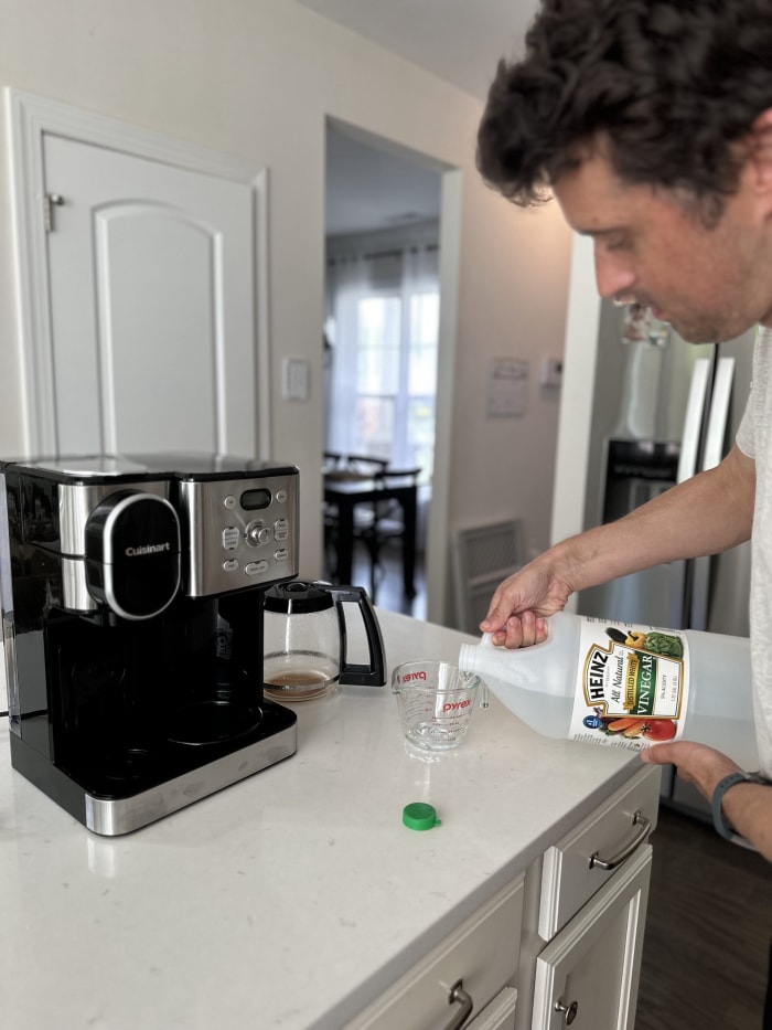 l'auteur verse du vinaigre dans une tasse à mesurer avec une cafetière sur le comptoir de la cuisine