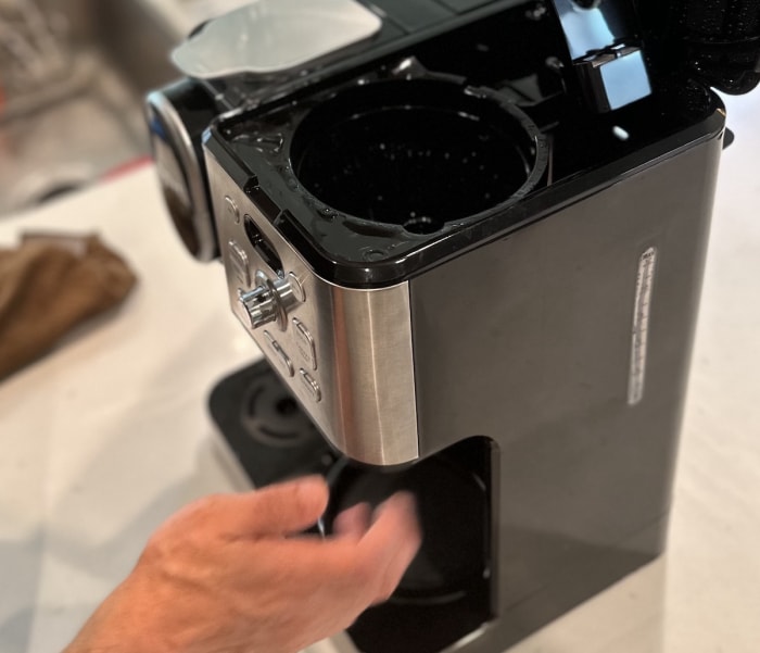 Cafetière automatique à filtre avec le dessus ouvert, exposant le réservoir. Un homme retire le filtre de la machine.