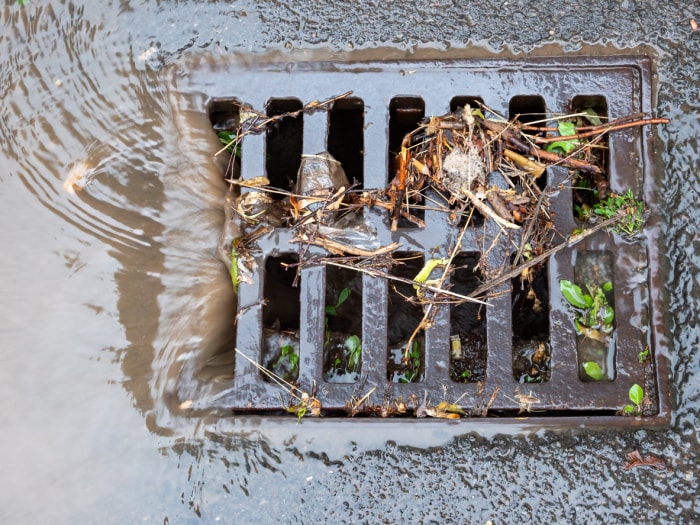 gros plan sur le gril carré d'un drain de bord de route avec écoulement d'eau et débris d'herbe