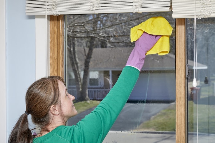 Une femme utilise un chiffon en microfibre jaune pour nettoyer une fenêtre à l'intérieur de sa maison.