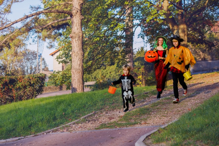 Une famille avec ses frères et sœurs court déguisée pour Halloween et tient un seau de bonbons dans le parc de la ville