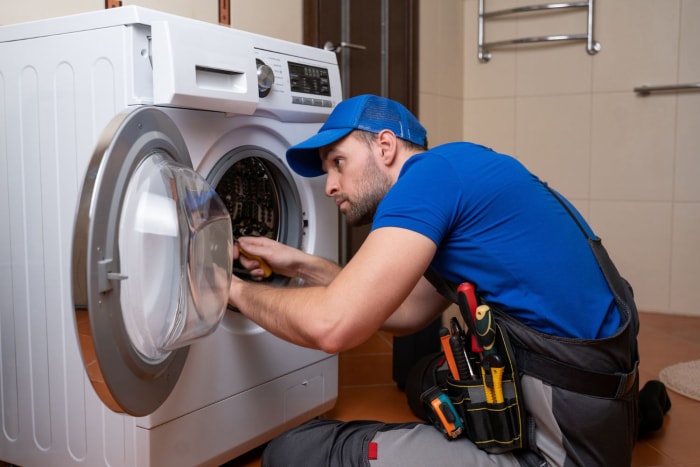 Un technicien habillé en bleu vérifie le fonctionnement d'une machine à laver. 