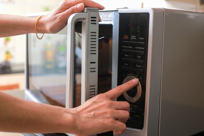 Les mains d'une femme ferment la porte du micro-ondes et appuient sur les boutons pour préparer les aliments.