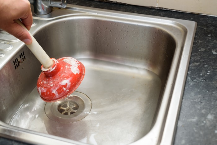 Homme utilisant une ventouse d'une seule main et de l'eau dans l'évier, utilisé pour nettoyer un évier de cuisine bouché/bloqué