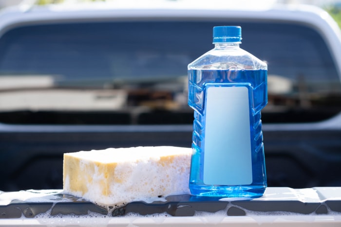 Gros plan d'un flacon de savon de lavage de voiture avec une éponge jaune pour le lavage, mise au point sélective