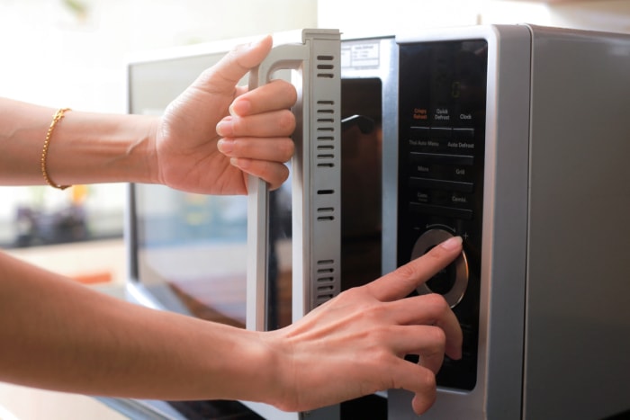 Mains d'une femme ouvrant un micro-ondes et utilisant des boutons