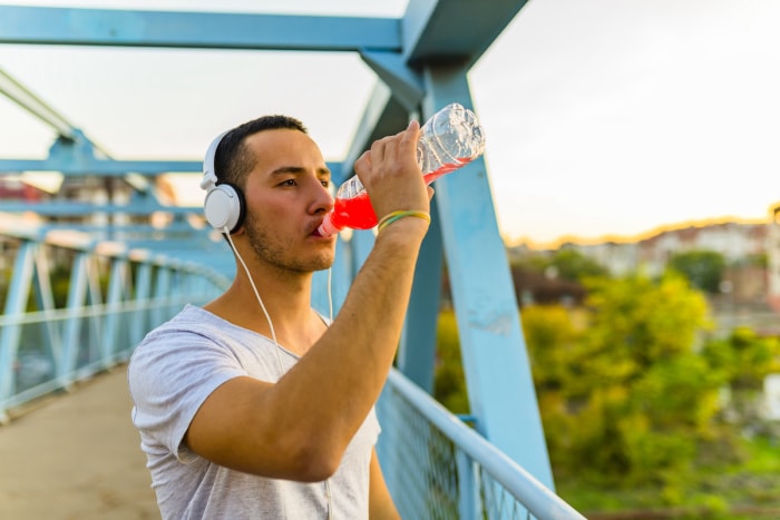 Jeune homme debout sur un pont buvant une boisson pour sportifs.