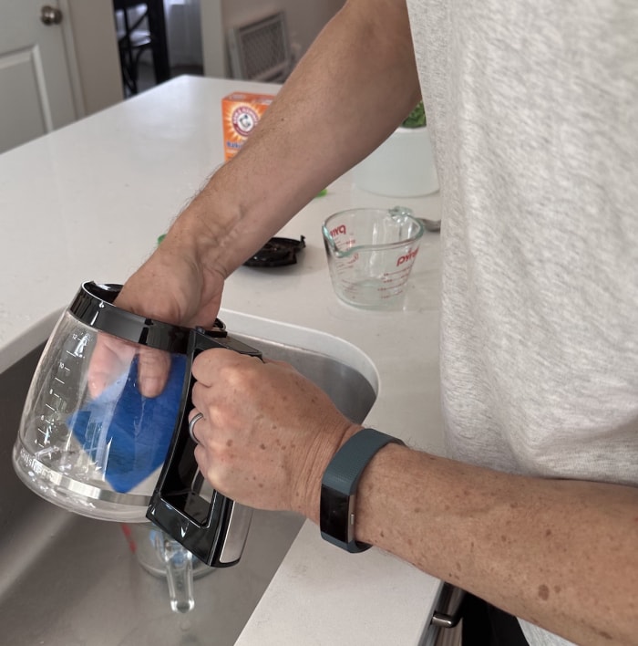 Homme lavant la carafe d'une cafetière avec une éponge