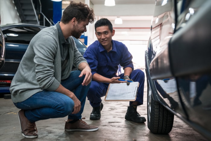 Un mécanicien automobile vérifie la roue de la voiture dans l'atelier de réparation automobile et parle avec le client.