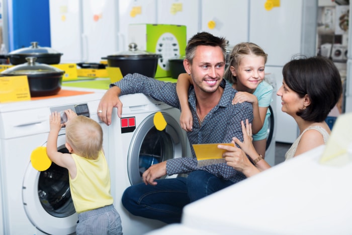 iStock-1070941210 vacances fiscales pour l'amélioration de l'habitat Des parents souriants avec des enfants achètent une machine à laver moderne