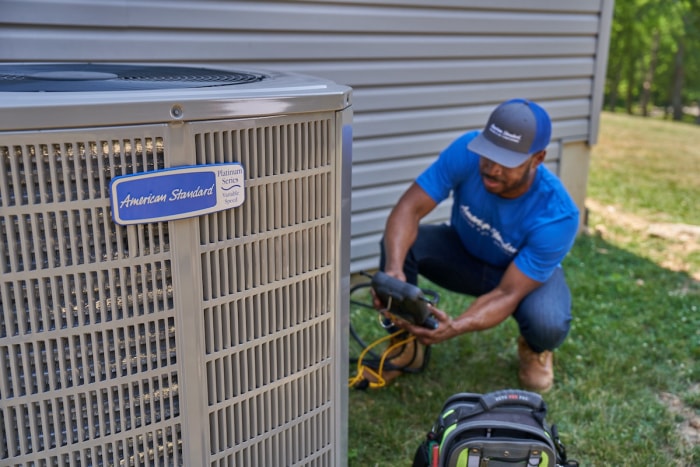 Un technicien HVAC d'American Standard installant une thermopompe résidentielle.