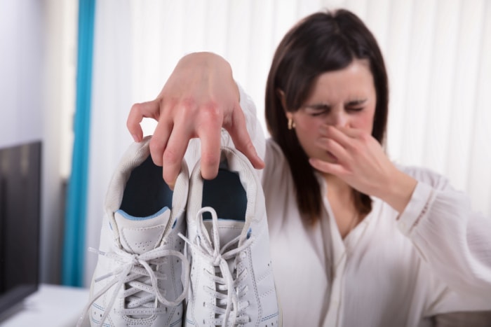 Une femme tenant des chaussures puantes et se tenant le nez