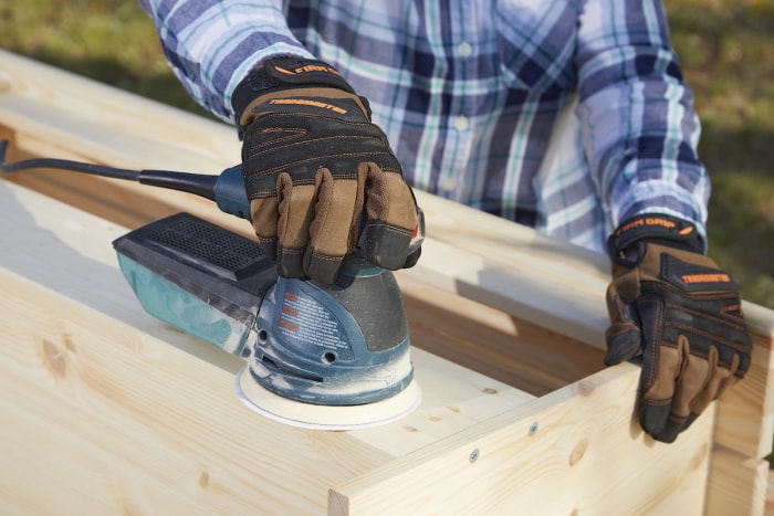 Une femme portant des gants de travail utilise une ponceuse à palettes pour poncer du bois.