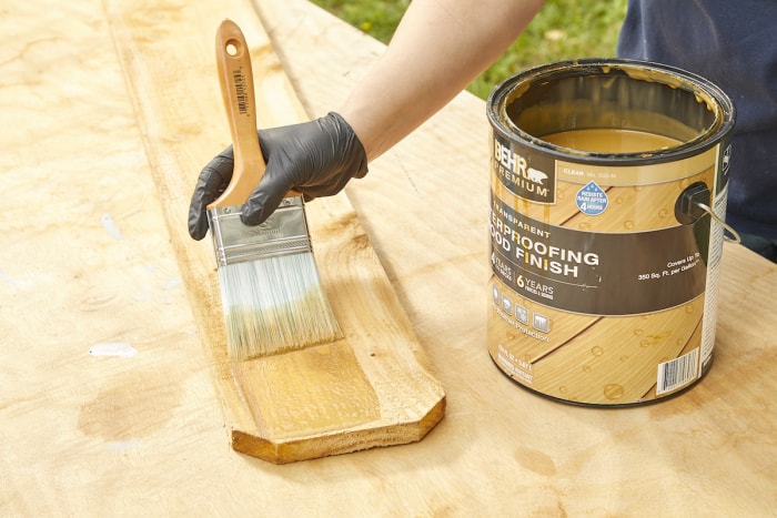 Une femme utilise un pinceau large pour teinter un 2x4 en bois traité sous pression.