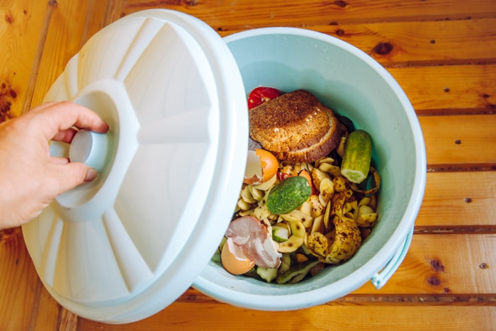 Personne mettant le couvercle sur un bac à compost de cuisine blanc rempli de restes de nourriture.