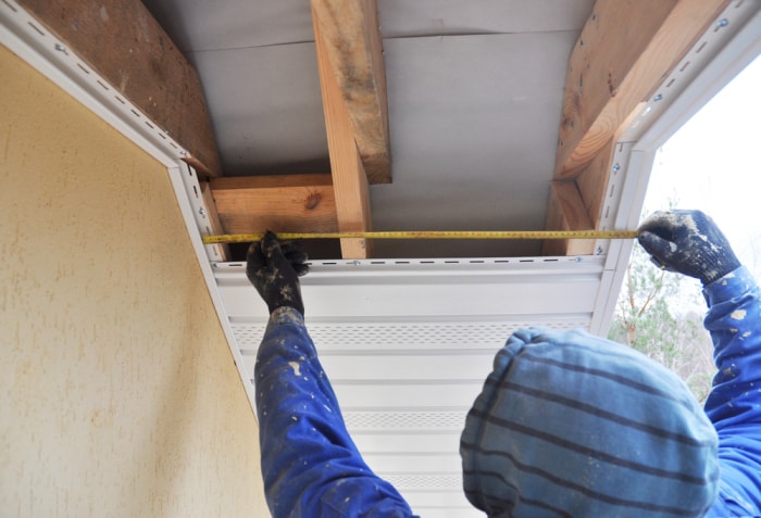 Un couvreur mesure le soffite à côté d'une maison.