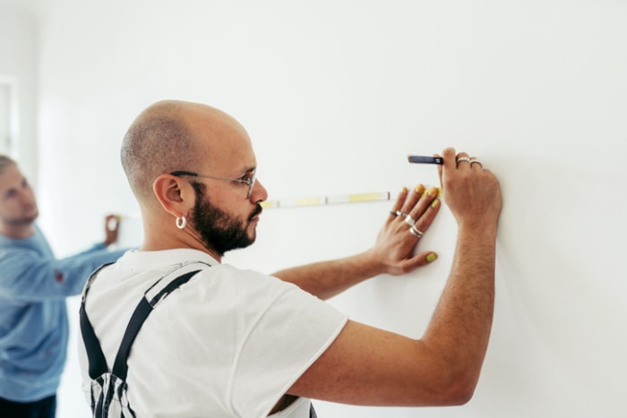 Homme faisant ses courses chez Home Depot et mesurant un mur avec un mètre ruban