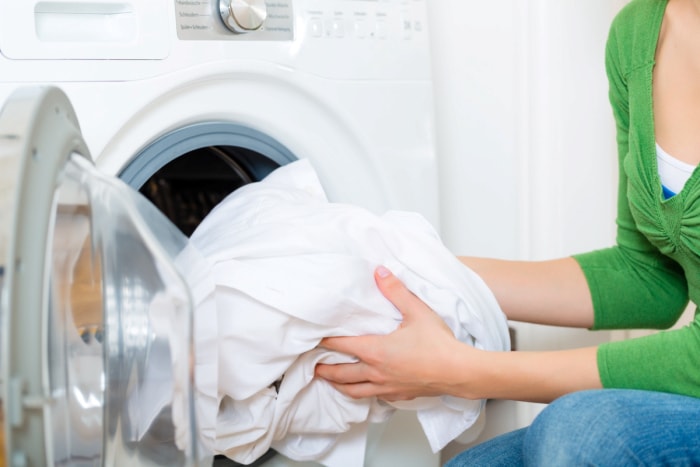 Personne mettant des draps blancs dans la sécheuse.