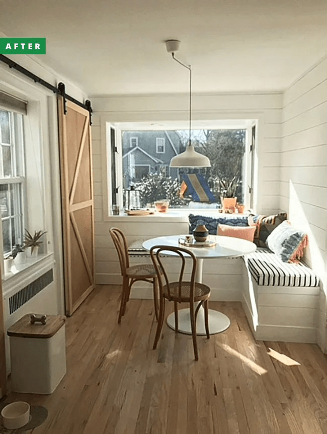 Un coin repas après rénovation avec une banquette et une porte de grange.