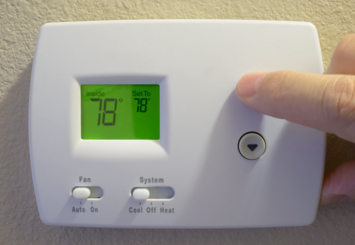 Personne réglant un thermostat numérique à 78 degrés Fahrenheit.