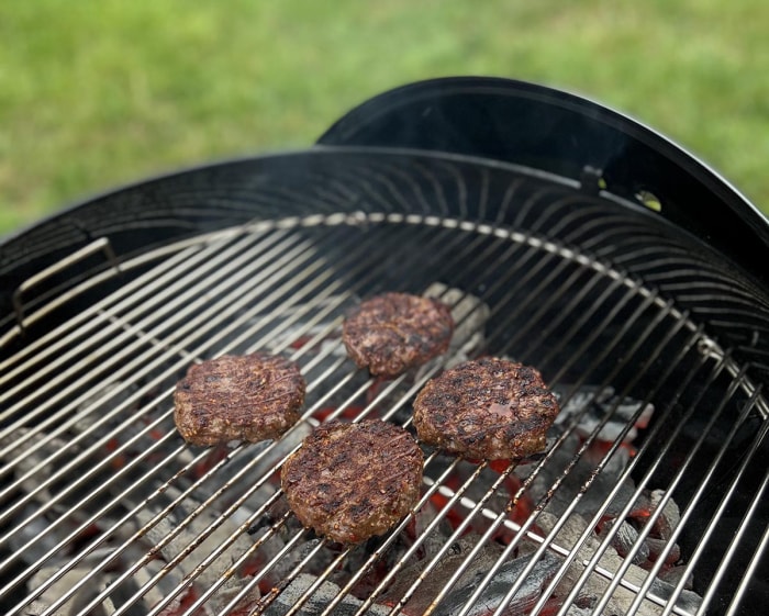 Le barbecue au charbon de bois Weber Original Kettle Premium en cours d'utilisation pour griller de la viande dans une cour