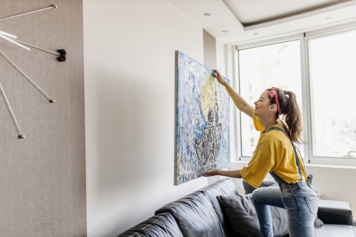 Jeune femme accrochant un tableau d'art au mur et décorant son salon