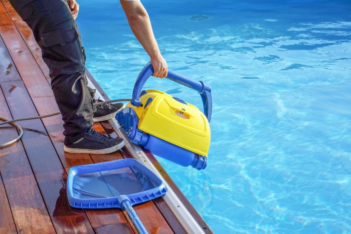 Un ouvrier place un aspirateur de piscine dans une piscine pour la nettoyer.