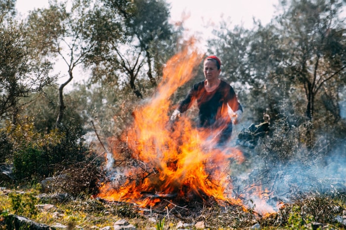 Une femme portant un bandana rouge s'occupe d'un tas de déchets de jardin en feu.