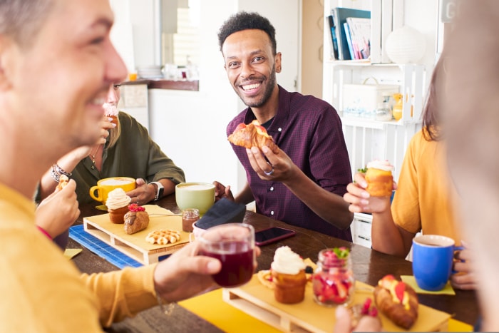 Des amis prennent leur petit-déjeuner en buvant des jus de fruits, du café et en mangeant des gâteaux. Des gens s'amusent à la cafétéria. Concept de style de vie et de communauté avec des hommes et des femmes heureux au café-bar. Photo de haute qualité