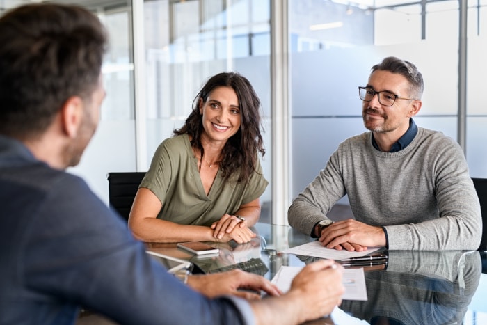 Un homme et une femme discutent avec un autre homme assis en face d'eux à une table dans un bureau. 