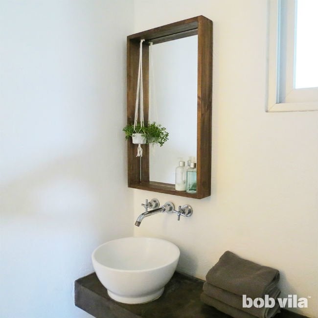 Miroir de salle de bain DIY encadré de bois avec une petite plante suspendue au-dessus d'un lavabo rond.