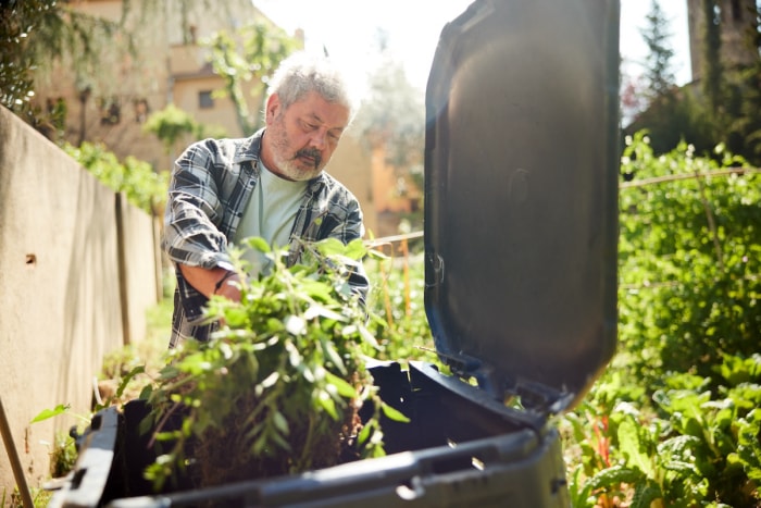 Un homme mûr jette des matériaux de compostage dans une poubelle. 