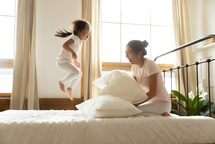 Le matin, une petite fille insouciante saute sur le lit tandis que la mère vietnamienne rit et se sent heureuse, une famille d'origine asiatique en pyjama confortable se réveille et commence une nouvelle journée avec une humeur positive et profite d'une vie active