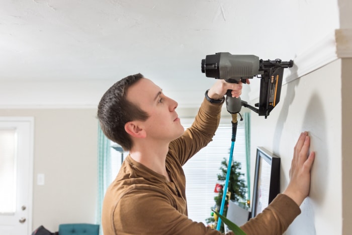 Un jeune homme utilise un pistolet à clous pour installer des moulures couronnées dans une maison.