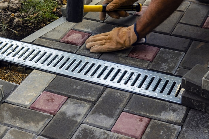 Installation d'un système de drainage en fer et de dalles de pavage. Gros plan d'une grille en fer le long du trottoir. Mise au point sélective.