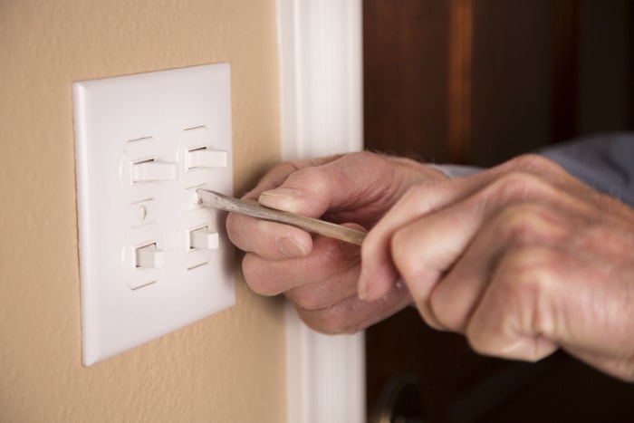 Une paire de mains utilise un tournevis pour installer une nouvelle plaque d'interrupteur.