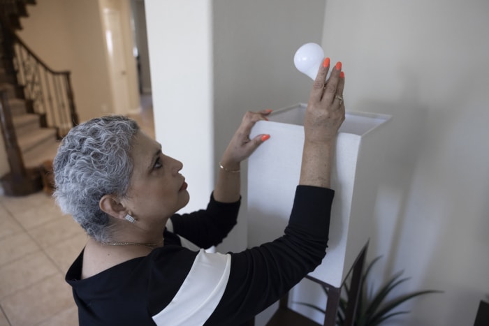 a-woman-holds-a-light-bulb-above-a-lamp-near near-a-staircase-in-the-home