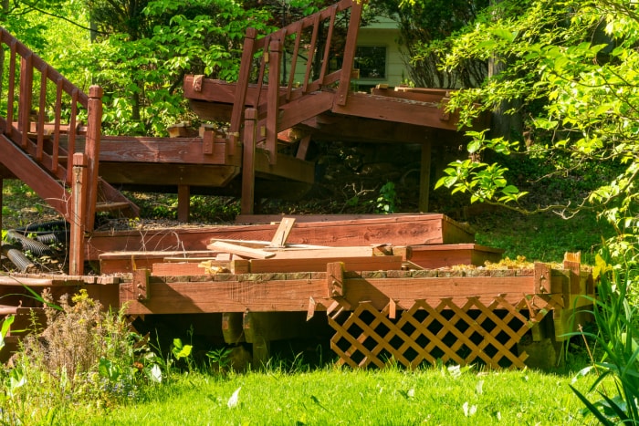 escalier-en-pont-cassé-avec-du-bois-pourri-et-des-rampes-tordues-devant-des-arbustes-verts