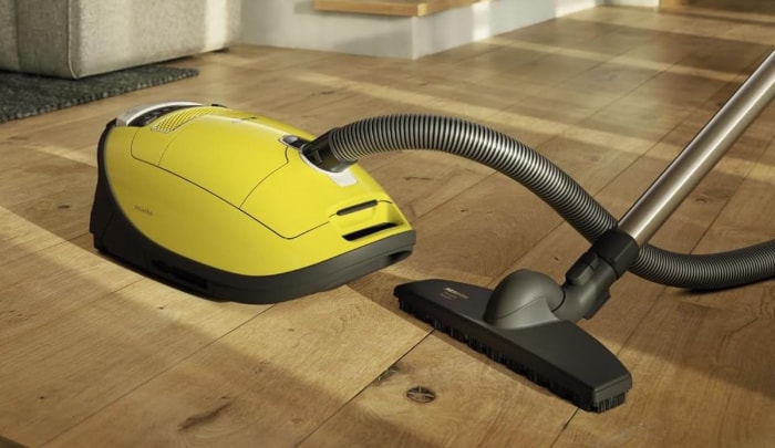 Un aspirateur-traîneau Miele Complete C3 Calima repose sur un plancher en bois dur avec la lumière du soleil qui brille dessus.