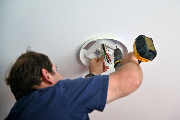 Personne utilisant une perceuse pour installer un luminaire.