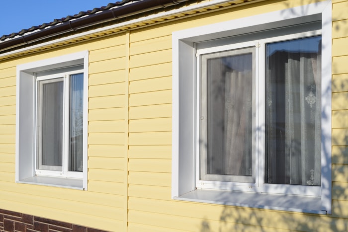 vue en angle du côté de la maison avec revêtement en vinyle jaune et deux fenêtres contre le ciel bleu