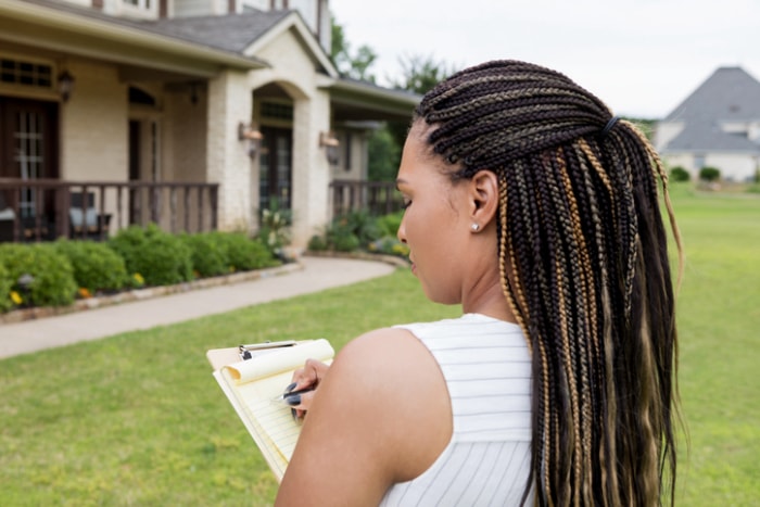 une-femme-avec-de-longues-tresses-regarde-son-bloc-notes-alors-qu'elle-se-tient-dans-la-cour-d'une-maison-bronzée