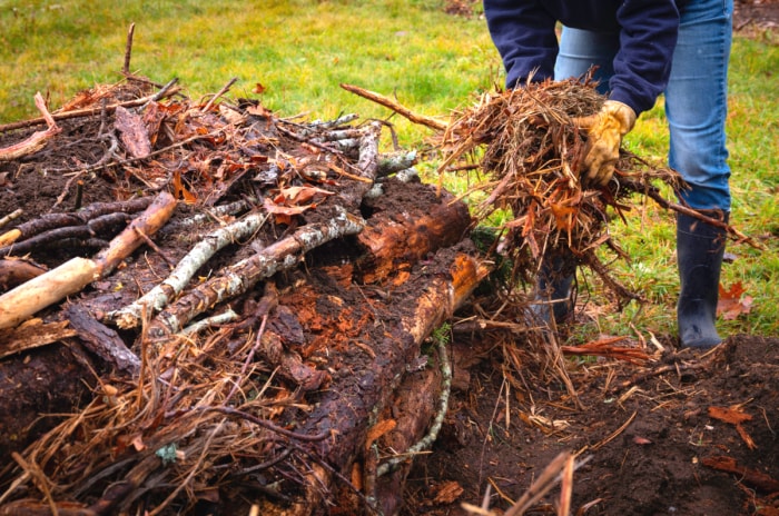 Un jardinier amateur ajoute des brindilles à un monticule de hugelkultur.