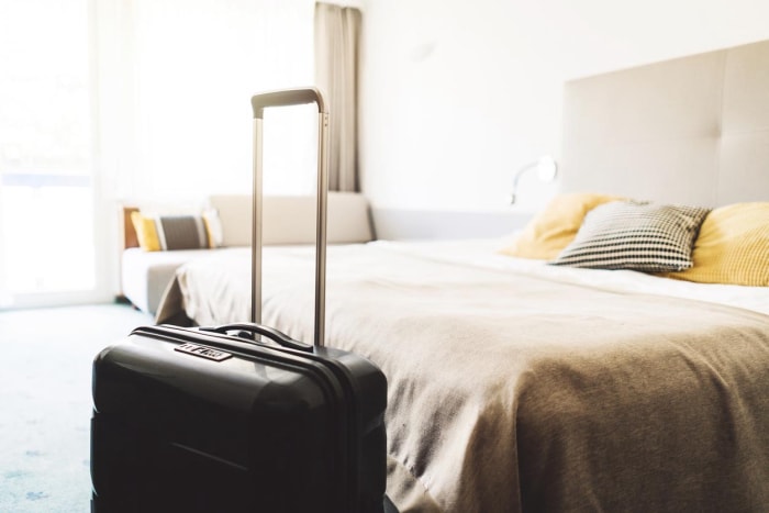 A suitcase sits on the floor at the end of a bed.