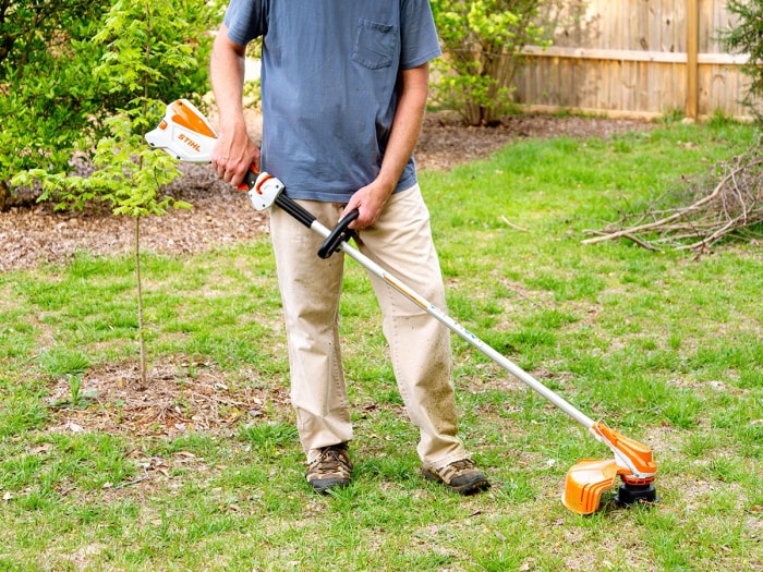 Personne coupant de hautes mauvaises herbes au milieu d'une cour avec un coupe-herbe Stihl